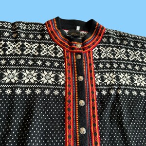 May include: A black cardigan sweater with a white snowflake pattern and a colorful trim. The sweater has a round neckline and is fastened with decorative buttons. The trim features red, orange, and blue stripes.