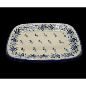 Könnte beinhalten: Ein rechteckiges Serviertablett aus Keramik mit abgerundeten Ecken, das eine cremefarbene Basis mit einem wiederkehrenden Muster aus kleinen blauen Blumen und grünen Stielen aufweist und mit einem dunkelblauen Rand am äußeren Rand versehen ist.