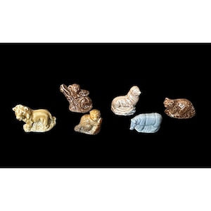 Puede incluir: Una colección de seis pequeñas figuras de animales de cerámica, que incluye un león beige, un oso marrón, un castor marrón, una foca beige claro, un hipopótamo azul claro y un animal marrón texturizado, todos con acabado brillante y moldeado.