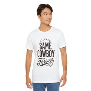 Könnte beinhalten: Weißes T-Shirt mit dem schwarzen Text "HITCHED SAME COWBOY Forever". Das Shirt hat einen Rundhalsausschnitt und kurze Ärmel. Das Design beinhaltet ein stilisiertes Hufeisen und eine Ringgrafik.