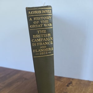 May include: A hardcover book titled "A History of the Great War" by A. Conan Doyle. The book's spine is olive green with gold lettering, detailing "The British Campaign in France and Flanders - 1915-". The publisher's name, DORAN, is at the bottom.