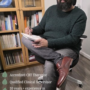 May include: A person with a beard wearing a dark green textured sweater and gray jeans, sitting in a chair while holding a pen and notebook. Text reads: Accredited CBT Therapist, Qualified Clinical Supervisor, 10 years + experience in Psychology and CBT, Founder of Making Therapy Simple.