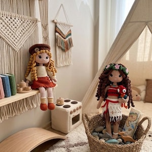 May include: Two handmade crochet dolls, one with curly blonde hair and a beret, the other with dark hair and a floral crown, sit in a child's room. The dolls are in a woven basket and on a shelf with other toys. The room has a neutral color scheme.