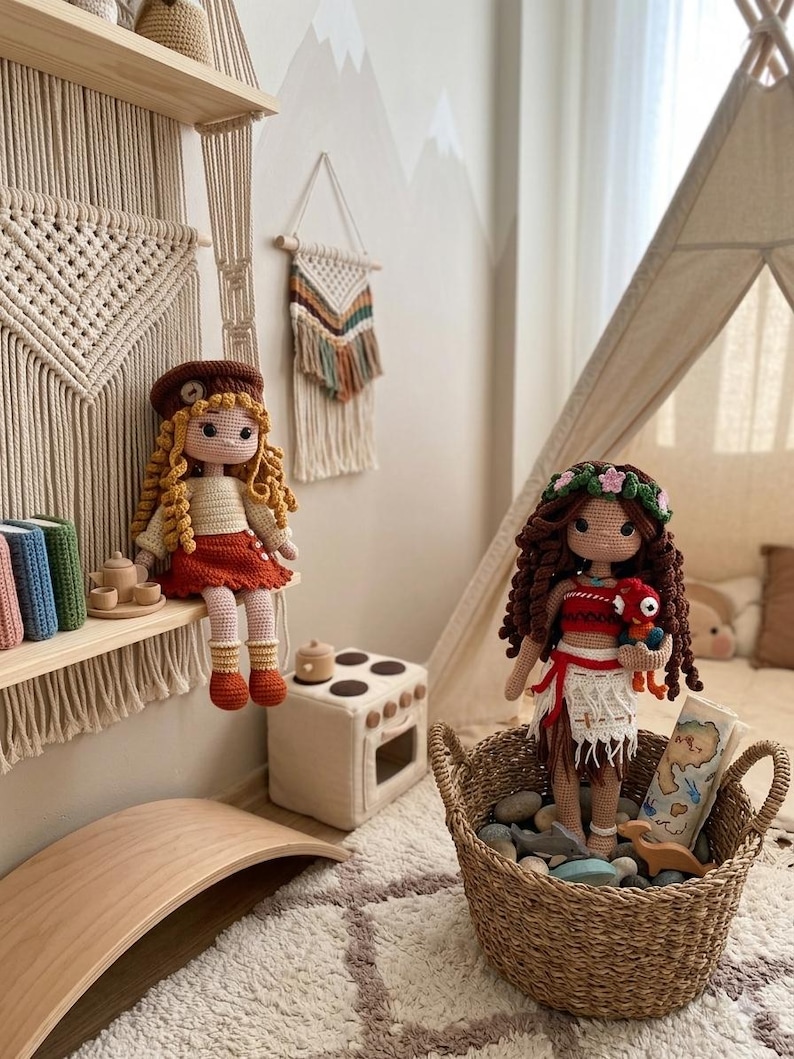 May include: Two handmade crochet dolls, one with curly blonde hair and a beret, the other with dark hair and a floral crown, sit in a child's room. The dolls are in a woven basket and on a shelf with other toys. The room has a neutral color scheme.