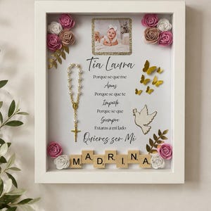 May include: A white shadow box frame containing a photograph of a baby, a pearl rosary, gold paper butterflies, a white dove cutout, and paper flowers in pink, white, and tan. The text reads: Tia Laura, Porque se que me Amas, Porque se que te Importo, Porque se que Siempre Estaras a mi lado, Quieres ser Mi MADRINA.