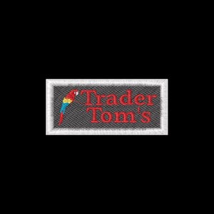 May include: A rectangular embroidered patch with a dark gray textured background and a white stitched border. The patch features a colorful parrot graphic on the left side and the red embroidered text Trader Tom's on the right side.