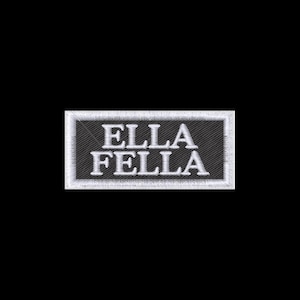 May include: A rectangular embroidered patch featuring a black background with a white border. The text ELLA FELLA is stitched in white capital letters across the center of the patch. The embroidery has a visible diagonal texture throughout the design.