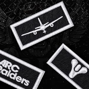May include: Three rectangular embroidered patches with white borders on a black background. One patch features a white airplane icon, another displays the text ARC RAIDERS with a rainbow stripe, and the third shows a white stylized emblem.