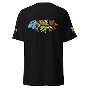 May include: Black t-shirt featuring a colorful graphic of cartoon characters with the text "Battle Waves". The design includes a blue rock monster, a fiery dragon, a blue ghost, a green creature, and a brown tree-like figure. A small green character is also on the sleeve.