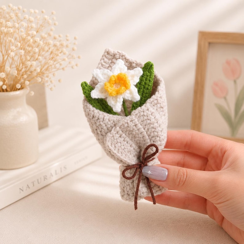 Crocheted narcissus daffodil flower with white petals and golden trumpet center surrounded by green leaves