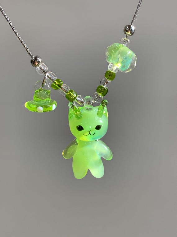 A handmade lampwork glass pendant of a little cat floating through space — tiny, surreal, and clearly made by a human with a torch.