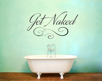 May include: A white bathtub with silver fixtures sits on a wooden floor in front of a light green wall. The wall has a black vinyl decal that reads "Get Naked" with a decorative swirl design.