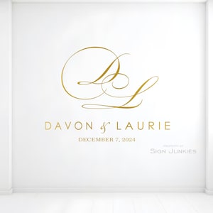 May include: A gold-colored wedding sign on a white wall. The sign features the names "Davon & Laurie" and the date "December 7, 2024" in a stylish font. The sign also includes a monogram and the text "PROPERTY OF SIGN JUNKIES".