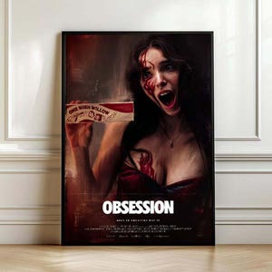 May include: A framed movie poster titled OBSESSION featuring a dark, dramatic scene of a person with a shocked expression, blood-like stains on their face and chest, and holding a rectangular box labeled ONE WISH WILLOW in a deep red and black color palette.
