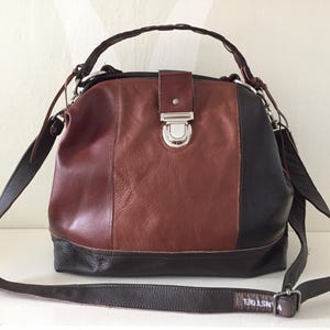 以下が含まれることがあります： 茶色、黒、バーガンディ色のトリコロールレザーハンドバッグ。シルバーの留め金、編み込みのトップハンドル、調節可能な長いショルダーストラップが付いています。ストラップには「ANSTDEL」の文字がプリントされています。