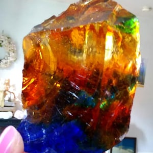 May include: A large, irregular chunk of translucent glass featuring a vibrant color gradient. The top section is a warm amber-yellow, transitioning through deep orange and red into a solid, saturated blue base with visible internal textures.