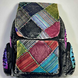Könnte beinhalten: Ein Rucksack mit Patchwork-Design auf der Frontklappe und Tasche, bestehend aus verschiedenen Samt- und Webstoffquadraten in Grün-, Blau-, Rot- und Violetttönen. Der Hauptkörper besteht aus dunkelgrauem Samt mit Seitentaschen und schwarzen Reißverschlüssen.