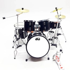 May include: Miniature black drum set with silver hardware and cymbals. The bass drum features the "dw" logo. The set includes a bass drum, snare drum, and two tom-toms, plus a hi-hat and a crash cymbal. A foot pedal is also included.