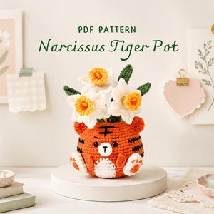 May include: A crochet PDF pattern titled Narcissus Tiger Pot featuring a bright orange tiger-shaped planter with black stripes, white belly, and small ears, holding a bouquet of white and yellow crocheted narcissus flowers with green leaves.