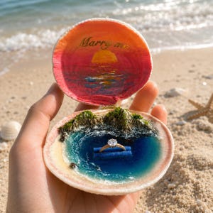 May include: A hinged seashell ring box featuring a hand-painted sunset scene with the text Marry me on the top interior. The bottom interior contains a miniature 3D landscape of rocky cliffs and blue water with a gold ring resting on a blue holder.