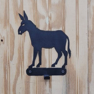May include: Black metal donkey silhouette wall hook. The hook is attached to a wooden wall.