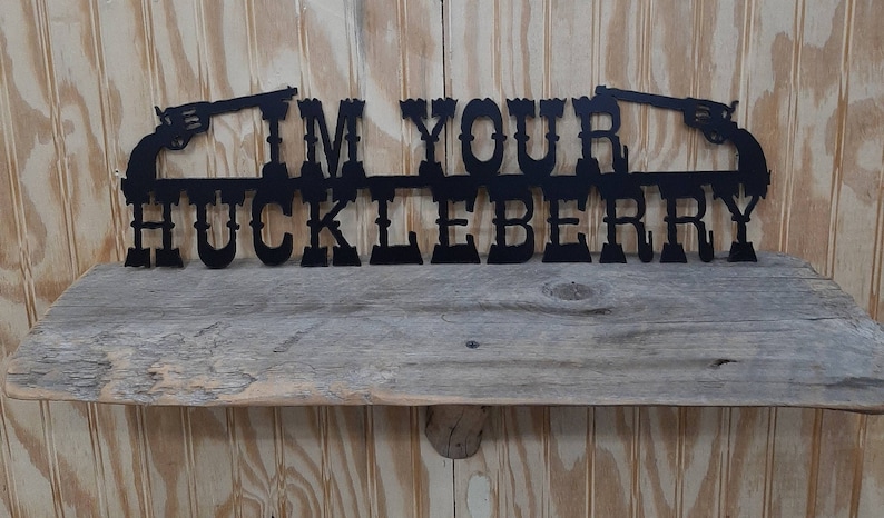 May include: Black metal wall decor with the text "I'm Your Huckleberry" and two pistols on either side.