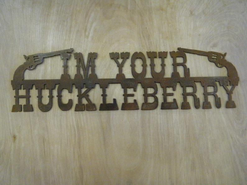 May include: Rustic metal sign with the text "I'm Your Huckleberry" and two stylized pistols on either side.
