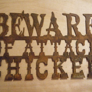 May include: Rusty metal sign with the words "Beware of Attack Chicken" in a decorative font.