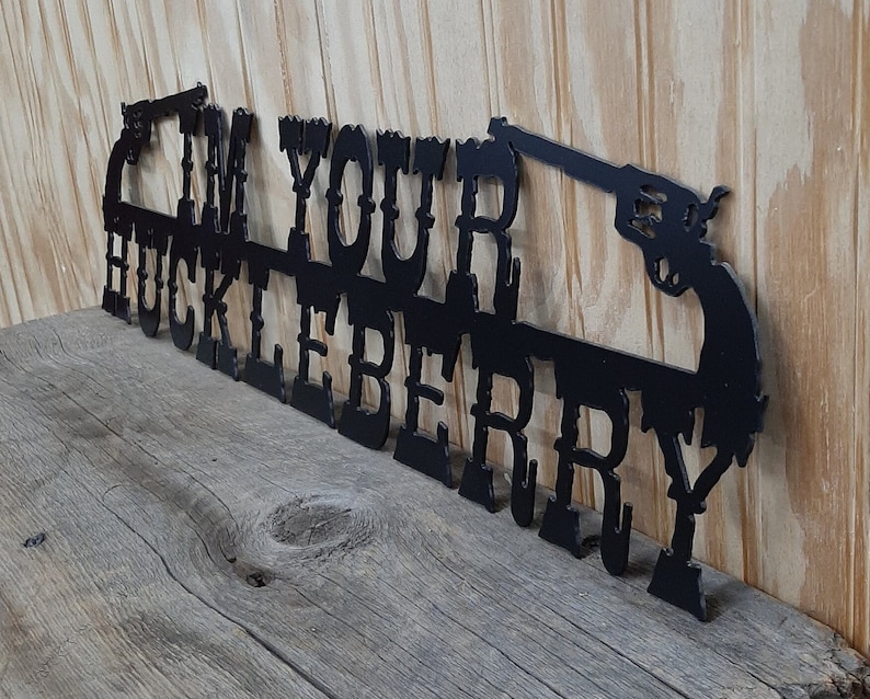 May include: Black metal wall decor with the text "I'm Your Huckleberry" and two stylized pistols.