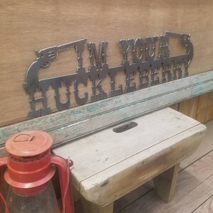 May include: Metal wall art with the text "I'm Your Huckleberry" and two stylized pistols on either side. The art is mounted on a wooden wall.
