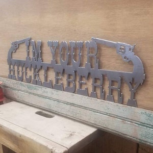 May include: Metal wall art with the text "I'm Your Huckleberry" and two stylized pistols. The art is painted in a silver color.
