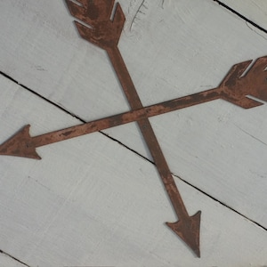 May include: Two rusty metal arrows crossed over each other on a white wooden background.