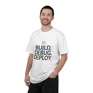 May include: White t-shirt with the words "BUILD. DEBUG. DEPLOY." in a black, blue, green, and red color scheme. The shirt also features a small graphic of a computer screen with code. The t-shirt is a short-sleeved, crew neck style.