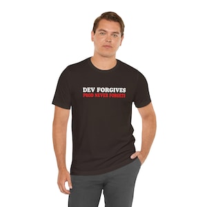 May include: A dark brown short-sleeve t-shirt featuring the white text "DEV FORGIVES" on the top line and the red text "PROD NEVER FORGETS" on the bottom line, centered on the chest area of the garment with a classic crew neckline design.