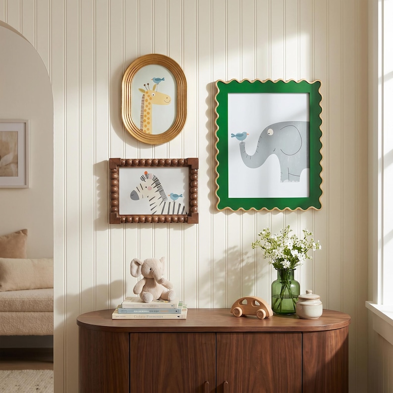 May include: A collection of framed animal art, including a giraffe, zebra, and elephant, each with a small blue bird. The frames are gold, green, and brown. A plush elephant toy and wooden car sit on a wooden cabinet.