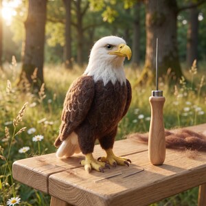 Op de afbeelding: Een naaldgevilte Amerikaanse zeearend-figuur met een witte kop, donkerbruin lichaam en gele snavel en klauwen. Naast de adelaar staat een viltgereedschap met een houten handvat en twee losse viltnaalden op het oppervlak.