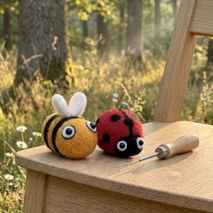 May include: A felted bee and ladybug sit on a wooden chair. The bee is yellow with black stripes and white antennae. The ladybug is red with black spots. A needle tool with a wooden handle rests nearby.