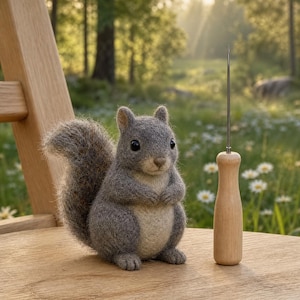 May include: A handcrafted gray felt squirrel with a fluffy tail sits on a wooden surface next to a wooden needle tool. The squirrel has a light-colored belly and dark eyes. The background features a blurred forest scene.