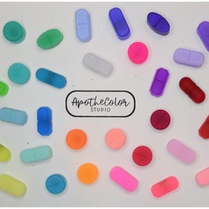 May include: A collection of small, colorful, pill-shaped and circular silicone beads in various shades including red, blue, green, yellow, pink, and purple. The text ApotheColor STUDIO is printed in black in the center of the arrangement.