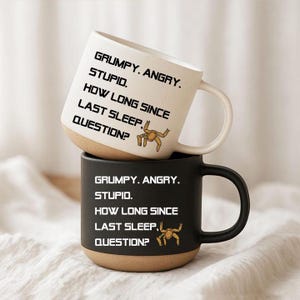 Peut inclure: Une tasse en céramique blanche empilée sur une tasse en céramique noire. Les deux tasses portent le texte "GRUMPY. ANGRY. STUPID. HOW LONG SINCE LAST SLEEP, QUESTION?" en caractères gras, accompagné d'un petit dessin de crabe brun aux pinces levées.