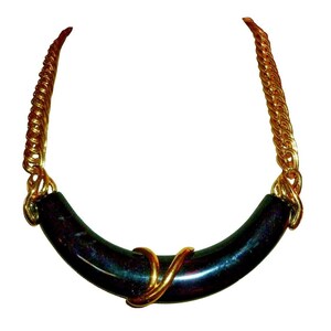 Könnte beinhalten: Eine goldfarbene Halskette mit einem gebogenen, dunkel gefärbten Mittelanhänger. Der Anhänger ist mit goldfarbenem Draht umwickelt. Die Kette hat ein gedrehtes Seildesign.