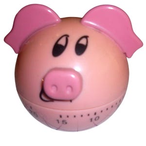 May include: A spherical kitchen timer shaped like a pig, featuring a light pink body, two darker pink ears, and a pink snout. The face includes black eyes and a black mouth. The lower section displays black numerical markings for time intervals.