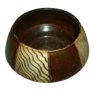 May include: A handmade ceramic bowl with a dark brown interior and exterior. The exterior features alternating panels of smooth, glossy brown and textured beige with wavy lines. The bowl has a rounded shape and is suitable for serving.