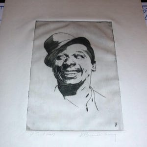 May include: A black and white etching of a smiling man wearing a hat. The artwork is signed and titled "V Trial Proof" and "J. Brandenburg". The man's face is detailed with visible lines and shading, capturing his expression.