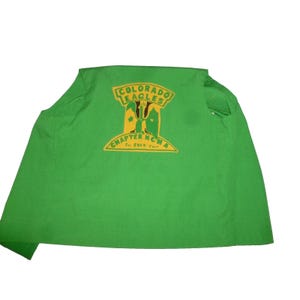 May include: A green garment with a yellow and black emblem that reads "COLORADO EAGLES CHAPTER NCM A Ft. COLO. Fort". The emblem features an eagle design. The garment is made of a lightweight material.