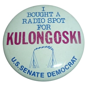 May include: A round, white political campaign button with blue and magenta text. The text reads "I BOUGHT A RADIO SPOT FOR KULONGOSKI U.S. SENATE DEMOCRAT." A blue graphic of radio towers is also present.