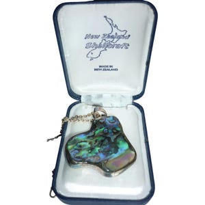 May include: A pendant necklace with a polished abalone shell pendant in a blue jewelry box. The pendant has iridescent colors of green, blue, and purple. The jewelry box is labeled "New Zealand Shellcraft".
