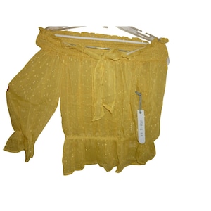 May include: A yellow off-the-shoulder blouse with long sleeves and a tie detail at the neckline. The blouse has a ruffled hem and is hanging on a white hanger. The fabric has a subtle, dotted pattern.