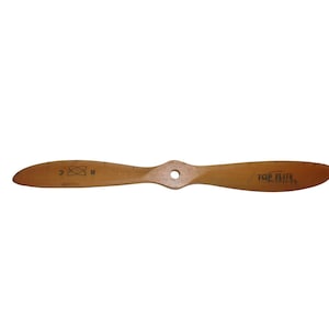 May include: A light brown wooden airplane propeller. The propeller has two blades and a central hub with a hole. The text "TOP ELITE" is printed on one blade. The other blade has the letters "R C" and a symbol. The propeller is a vintage item.