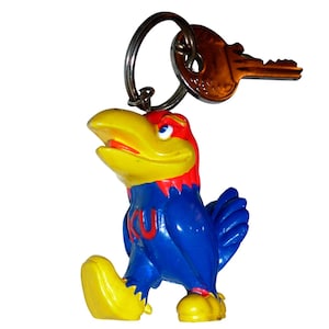 May include: A keychain featuring a molded plastic bird figure with a yellow beak and feet, a red head, and a blue body with the letters KU in red on the chest. The figure is attached to a silver metal split ring that holds a single metal key.